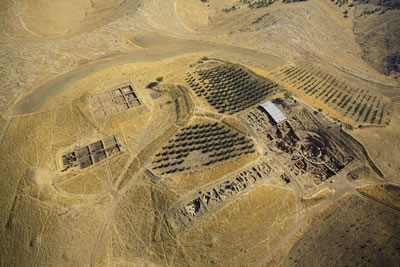 <p><strong>1. </strong>Göbekli  Tepe Dünya Miras Alanının, 2011 yılında koruyucu çatıların yapımından önce havadan  görünümü. Höyük, yüksek tepelerden ve daha alçak çukurlardan oluşan bir  yerleşim silsilesi sunmaktadır. Ana kazı alanından (güneydoğuda yer alan çukur;  sağda ortada) höyüğün güneybatısı boyunca, batıya doğru yayılan sekiz kazı  alanı yer almaktadır. Höyüğün kuzeybatısında, ilerleyen çalışmaların  gerçekleştirildiği yükselti (solda üstte) ve çukur (solda ortada)  bulunmaktadır.</p>